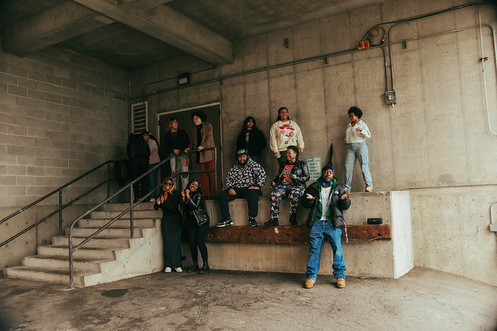 The Black Student Coalition posing together on a stairway in the corner of a building's concrete exterior