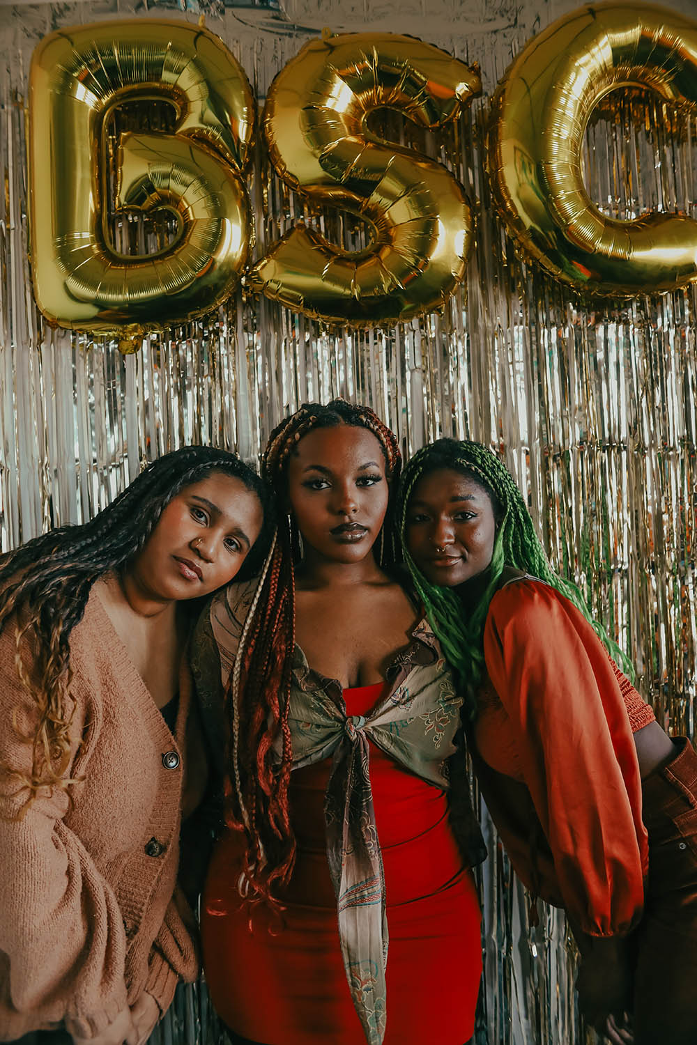 Three Black women with colorful braids pose together under gold "BSC" balloons