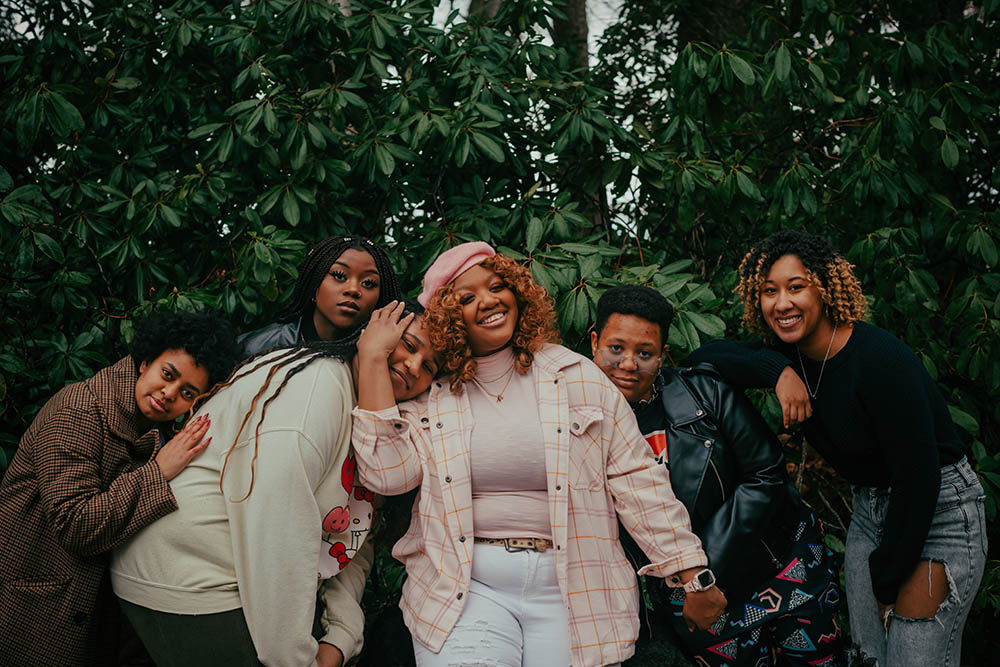 A group of women from the Black Student Coalition embracing and posing happily in front of dark green foliage