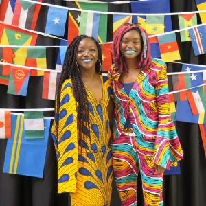 Two Black students in brightly colored suits standing in front of international flags